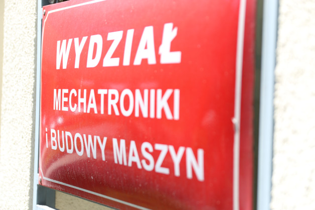 Czerwona tablica z białym napisem "WYDZIAŁ MECHATRONIKI I BUDOWY MASZYN".
