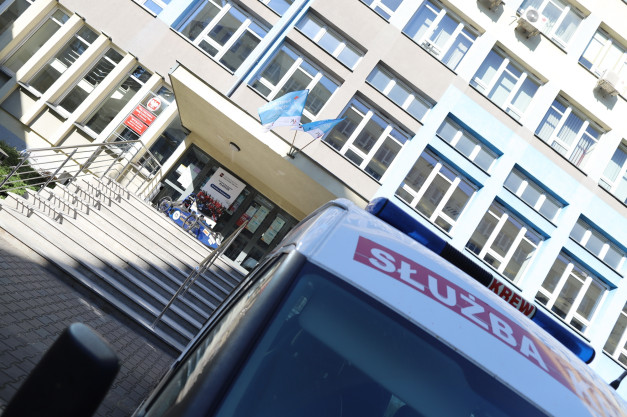 Samochód służbowy z napisem "SŁUŻBA KREW" przed budynkiem uczelni.