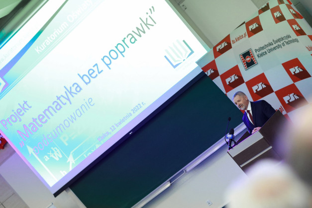 Mężczyzna w garniturze przemawia na tle ekranu z napisem "Projekt Matematyka bez poprawek" i logo Politechniki