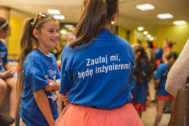 Dziewczynki w niebieskich koszulkach z napisem "Zaufaj mi, będę inżynierem!". Kontekst: wydarzenie edukacyjne.