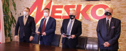 Czterech mężczyzn w garniturach i maseczkach stoi przed ścianą z logo MESKO i PGZ.