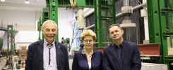 Trzy osoby stoją przed maszynami w laboratorium. Widać betonowe elementy i zielone konstrukcje.