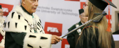 Uroczystość wręczenia dyplomów. Mężczyzna w todze wręcza berło absolwentce. Kontekst: ceremonia akademicka.