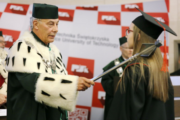 Uroczystość wręczenia dyplomów. Mężczyzna w todze wręcza berło absolwentce. Kontekst: ceremonia akademicka.