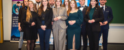 Grupa młodych ludzi pozuje do zdjęcia przed banerem KRD. Wszyscy ubrani są formalnie.