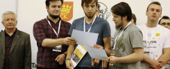 Mężczyźni w koszulkach i marynarkach stoją przed napisem "ORGANIZATORZY". Trzymają dokumenty i torby.