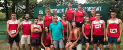 Grupa sportowców w strojach sportowych pozuje do zdjęcia na tle zielonego banera. W tle widać drzewa.