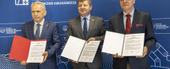 Trzech mężczyzn w garniturach pozuje z dokumentami przed niebieskim tłem z logo Politechniki Rzeszowskiej.