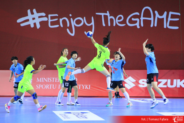 Piłka ręczna: zawodniczki w neonowych i niebieskich strojach rywalizują na boisku. W tle napis #EnjoyTheGAME.