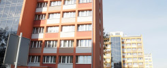 Pomarańczowy budynek mieszkalny z oknami i szklaną fasadą. W tle inne budynki.