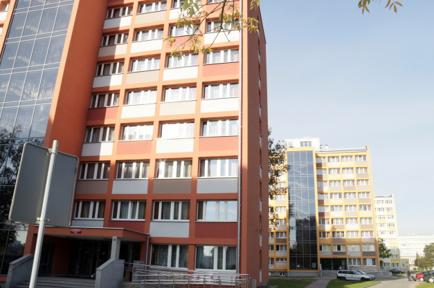 Pomarańczowy budynek mieszkalny z oknami i szklaną fasadą. W tle inne budynki.