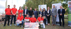 Grupa osób w czerwonych koszulkach i garniturach pozuje z dyplomami i nagrodami pieniężnymi.