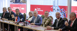 Ludzie siedzą przy stole konferencyjnym z flagami i mikrofonami. Kontekst: spotkanie w Politechnice Świętokrzyskiej.