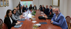 Grupa osób siedzi przy stole konferencyjnym. Na stole są dokumenty, napoje i przekąski.