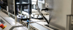 Automatyczna linia produkcyjna z taśmociągiem, elementami maszyn i przyciskiem awaryjnym. Kontekst: przemysł, produkcja.