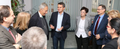 Grupa osób rozmawia w pomieszczeniu. Widać mężczyzn w garniturach i kobiety w eleganckich strojach.
