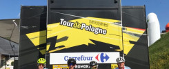 Czterech kolarzy w strojach z logo "Tour de Pologne" stoi obok ciężarówki z banerami "Muzeum Tour de Pologne".