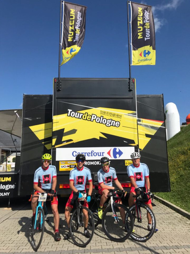 Czterech kolarzy w strojach z logo "Tour de Pologne" stoi obok ciężarówki z banerami "Muzeum Tour de Pologne".