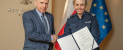 Mężczyzna w garniturze i kobieta w mundurze policji podają sobie ręce. Trzymają dokument.