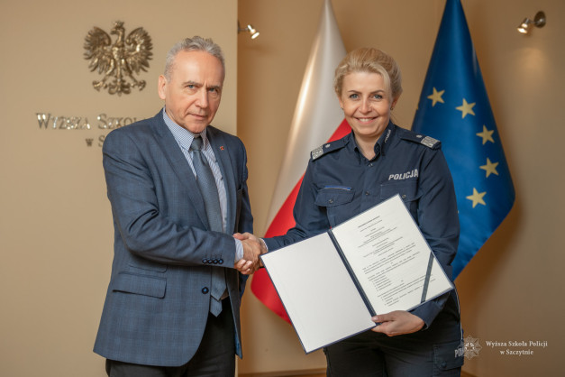 Mężczyzna w garniturze i kobieta w mundurze policji podają sobie ręce. Trzymają dokument.