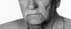 Portret starszego mężczyzny z wąsami, ubranego w marynarkę i czarną koszulkę.