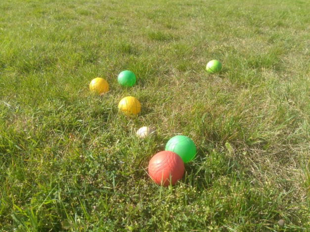 Na trawie leżą kolorowe kulki do gry w bule. Są zielone, żółte, czerwona i biała.