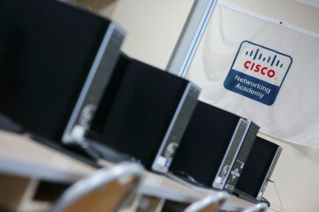Rząd komputerów z logo Cisco Networking Academy. Kontekst: sala lekcyjna lub pracownia komputerowa.