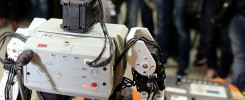 Robot z modułem sterującym i okablowaniem. W tle widać ludzi.