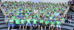 Grupa dzieci w zielonych koszulkach i okularach 3D siedzi na widowni. Kontekst: wydarzenie edukacyjne lub pokaz.