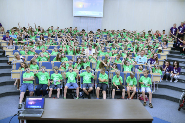 Grupa dzieci w zielonych koszulkach i okularach 3D siedzi na widowni. Kontekst: wydarzenie edukacyjne lub pokaz.