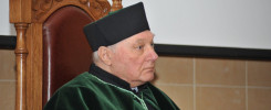 Starszy mężczyzna w togach akademickich siedzi na ozdobnym krześle.