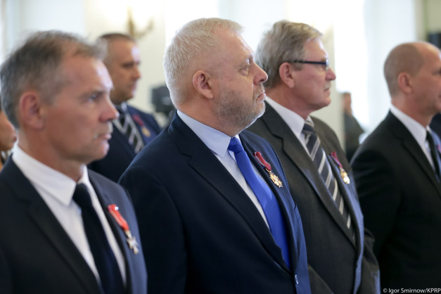 Mężczyźni w garniturach i z odznaczeniami stoją w rzędzie. Uroczystość państwowa.
