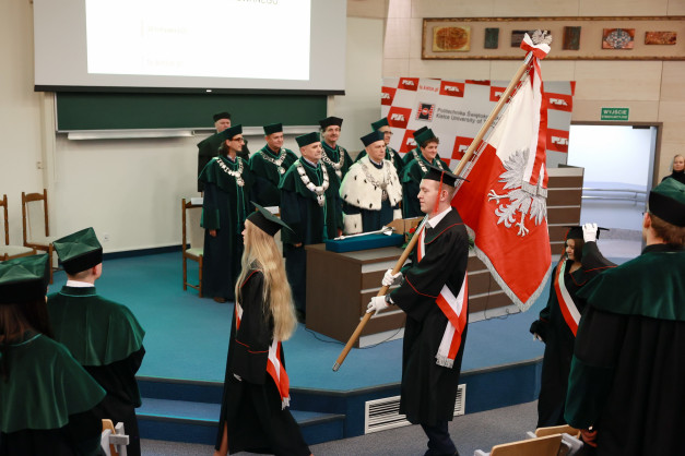 Uroczystość akademicka z udziałem osób w togach i biretach. Kluczowe obiekty: togi, birety, polska flaga.