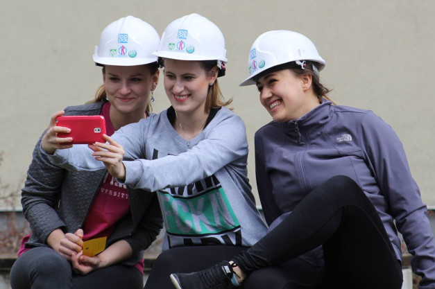 Trzy kobiety w białych kaskach robią selfie. Kobiety, kaski, telefon, kurtki.