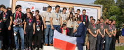 Grupa młodych ludzi na podium z pucharem i flagą Polski. Kontekst: ceremonia wręczenia nagród.