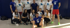 Grupa młodych ludzi w strojach sportowych pozuje do zdjęcia na tle baneru z logo.