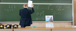 Nauczyciel pisze równania matematyczne na zielonej tablicy. Widać wzory, liczby i napisy.