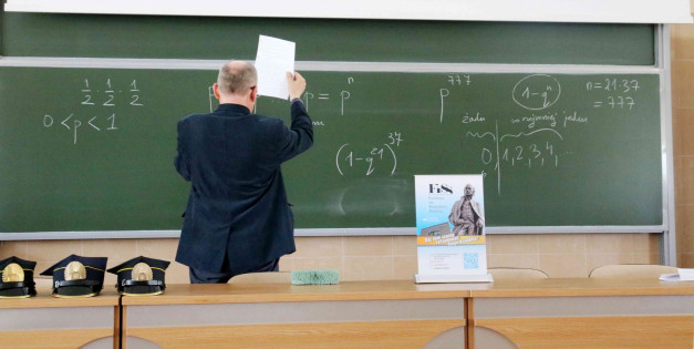 Nauczyciel pisze równania matematyczne na zielonej tablicy. Widać wzory, liczby i napisy.