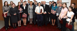 Grupa osób w strojach formalnych stoi na czerwonym dywanie, trzymając dyplomy.