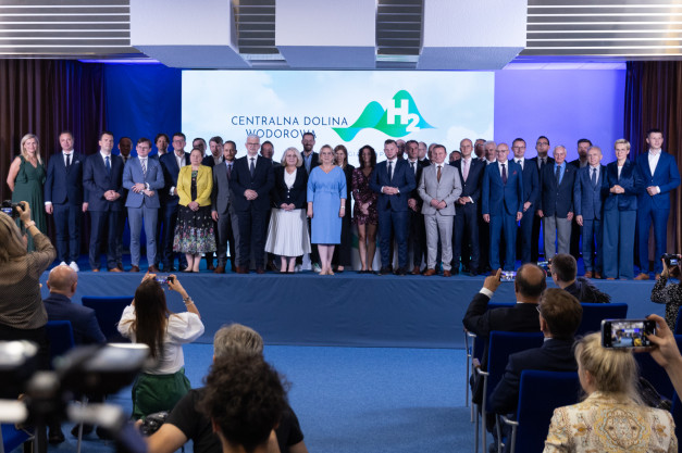 Grupa osób w strojach formalnych stoi na scenie przed ekranem z logo "Centralna Dolina Wodorowa H2".