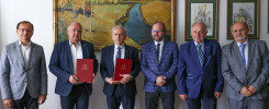 Sześciu mężczyzn w garniturach stoi przed obrazem. Trzech z nich trzyma czerwone teczki.