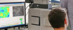 Dwóch mężczyzn pracuje przy mikroskopie i komputerze z analizą danych. Kluczowe obiekty: mikroskop, monitor, klawiatura, mysz.