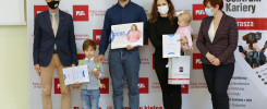 Osoby w strojach galowych stoją na tle Politechniki Świętokrzyskiej, trzymając dyplomy i nagrody.