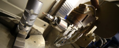 Metalowy element z wycięciami w uchwycie maszyny CNC. W tle widoczna głowica robocza.