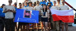 Grupa osób trzyma polską flagę i baner Politechniki Świętokrzyskiej. Kluczowe obiekty: ludzie, flaga, baner, budynek.