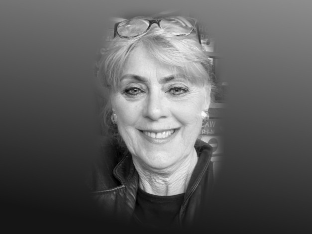 Portret kobiety z okularami na głowie, uśmiechniętej. Kluczowe obiekty: kobieta, okulary, kurtka. Kontekst: zbliżenie.