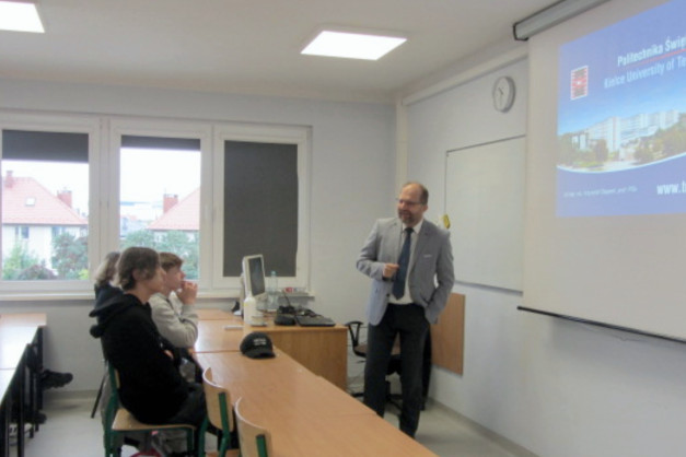 Mężczyzna w garniturze prezentuje na ekranie Politechnikę Świętokrzyską. W sali są studenci.