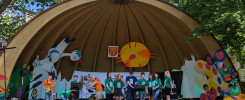 Zespół muzyczny występuje na scenie pod zadaszeniem. Kluczowe obiekty: scena, muzycy, instrumenty, kolorowe dekoracje.