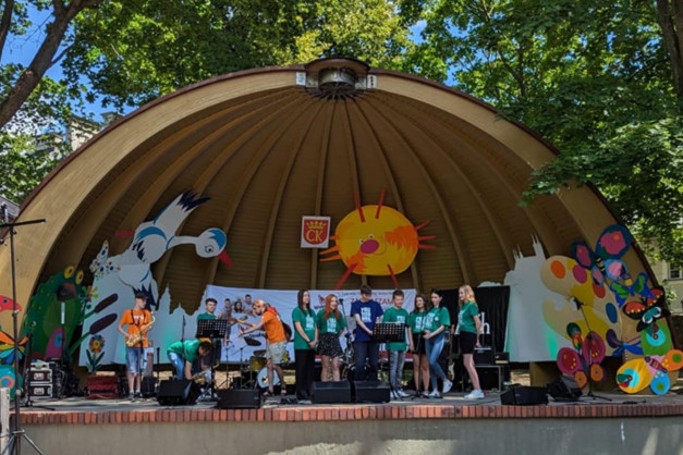 Zespół muzyczny występuje na scenie pod zadaszeniem. Kluczowe obiekty: scena, muzycy, instrumenty, kolorowe dekoracje.