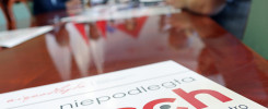 Na stole leży materiał z napisem "niepodległa tech". W tle widać ludzi siedzących przy stole.